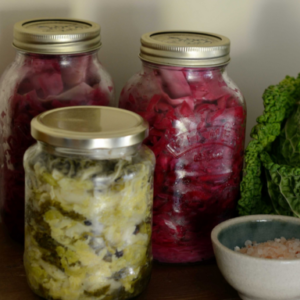 A jar of red pickled cabbage and a jar of green pickled cabbage placed on a rustic wooden table.