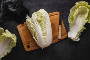 fresh Chinese cabbage on a wooden chopping board with a sharp knife beside it, ready for slicing.